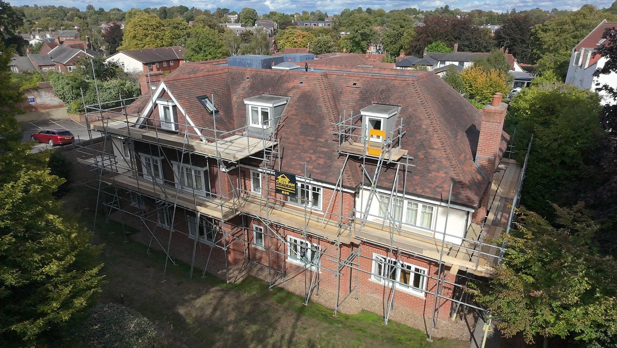 Drone view of a large dormered house with scaffold to the eaves and platforms at each dormer