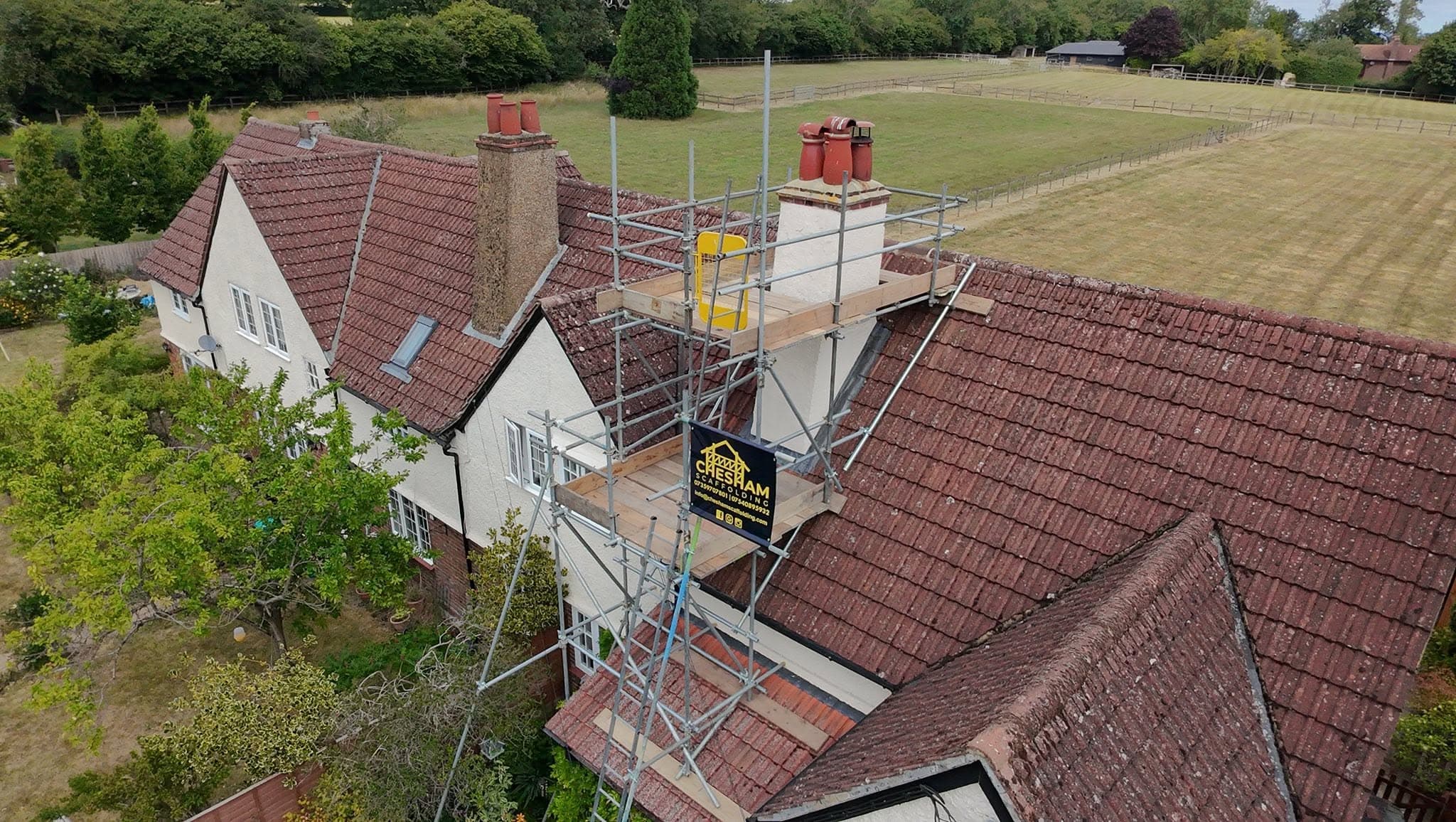 Drone view of a chimney scaffold on a tiled roof with fields behind