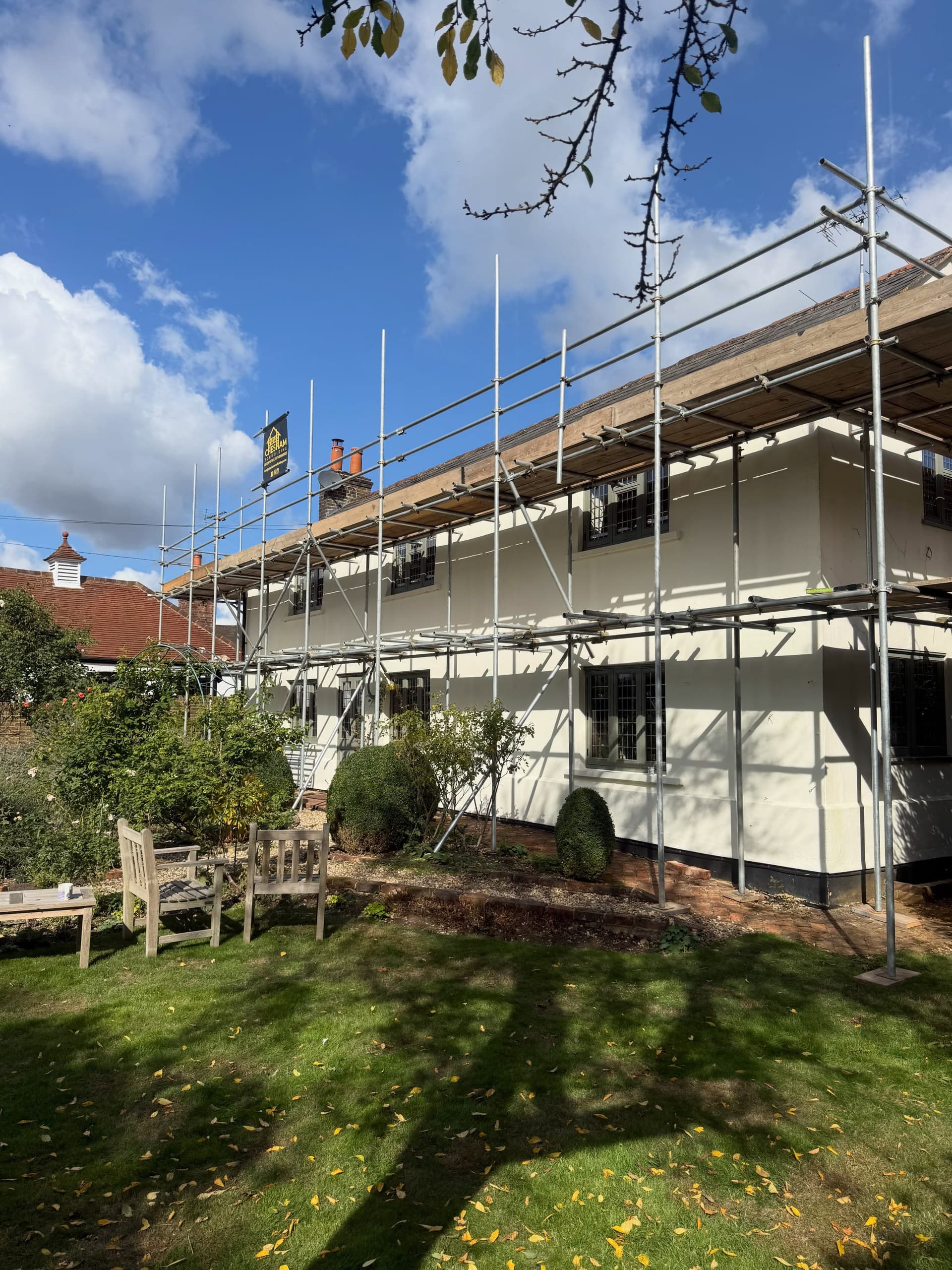 Long rendered cottage with scaffold to the eaves and a Chesham Scaffolding board, under a blue sky