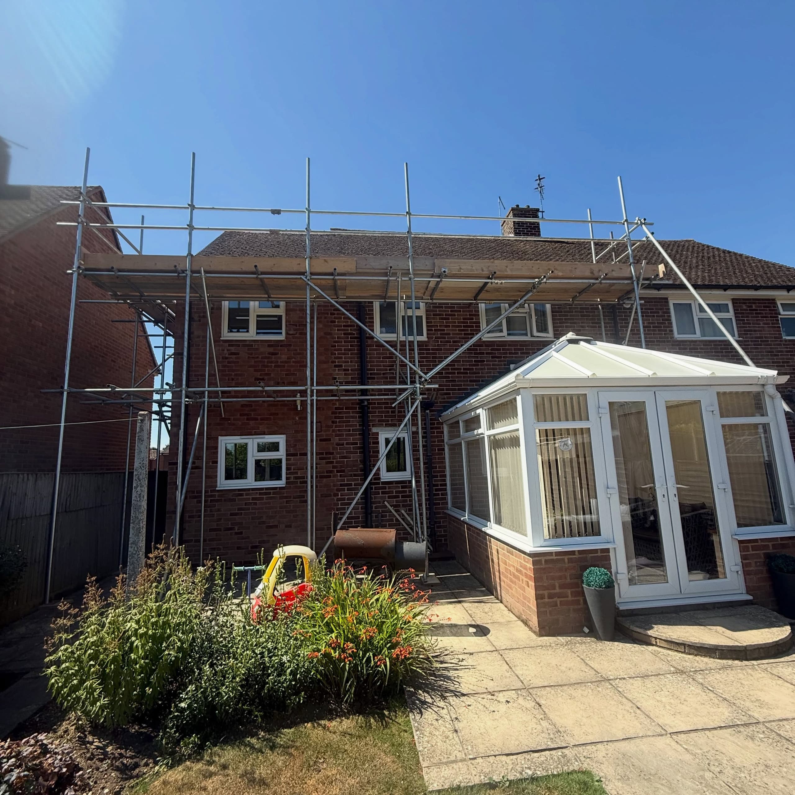 Rear of a semi with scaffold bridged over the conservatory, garden and patio left clear