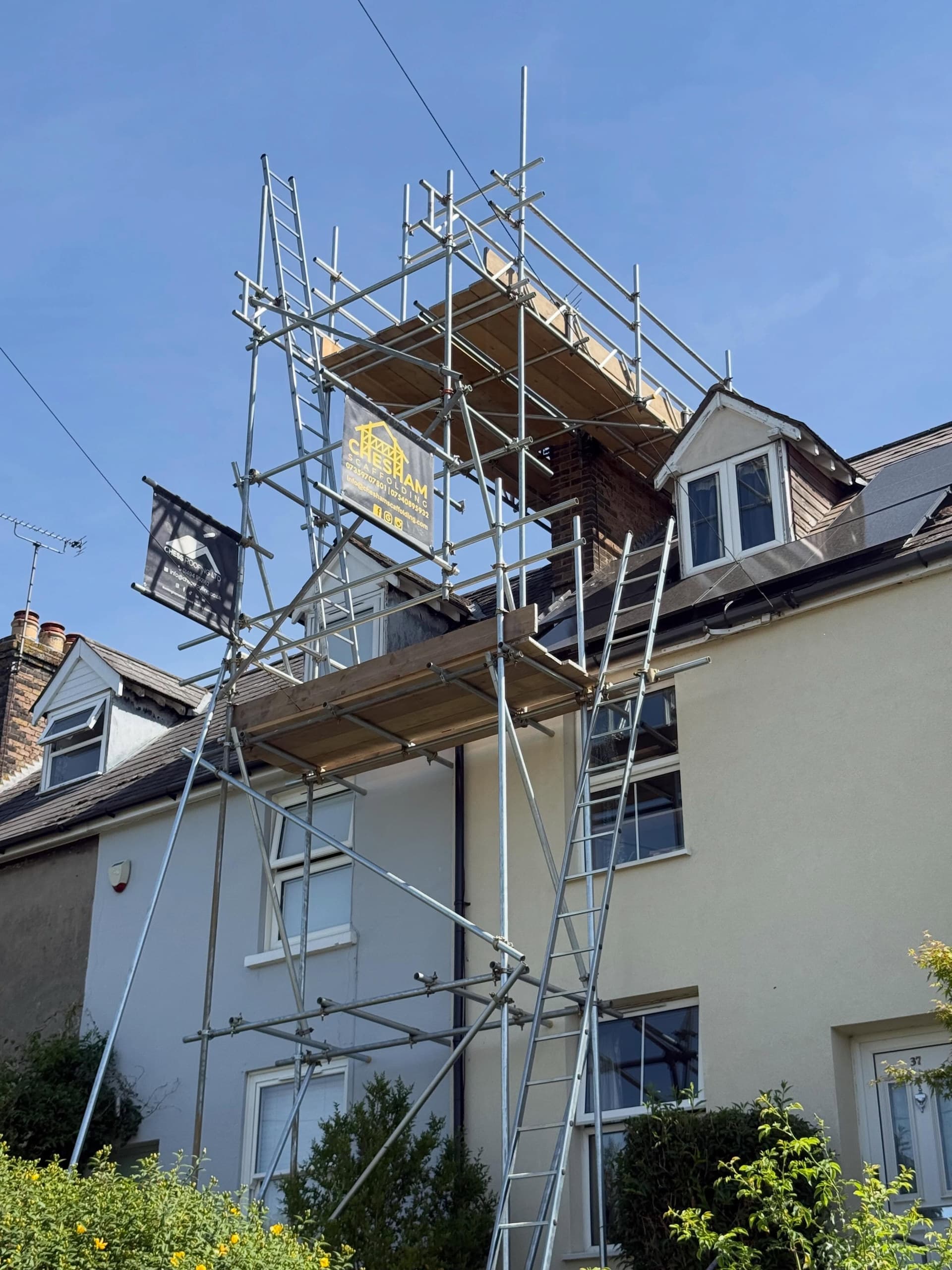 A long Chesham Scaffolding scaffold run to the eaves of a cottage, company board flying, under a blue sky