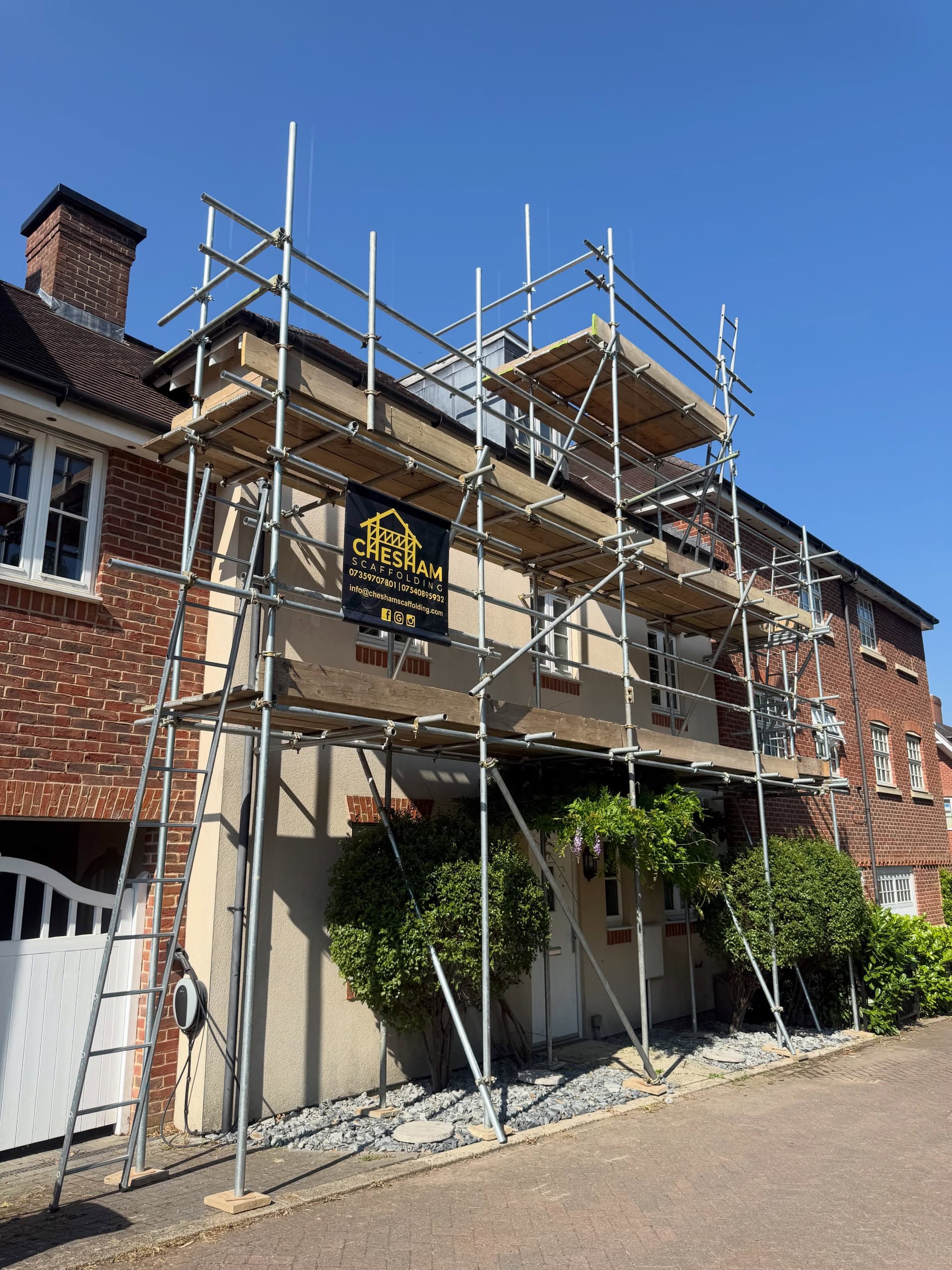 Tall scaffold up a three-storey townhouse with a company board against a deep blue sky